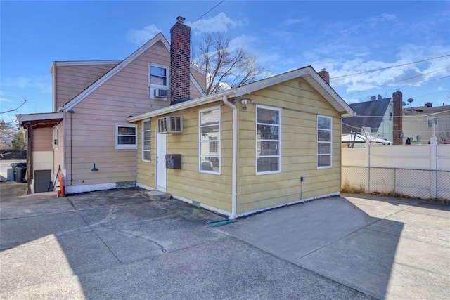 rear view of house with cooling unit, a wall mounted air conditioner, fence, a chimney, and a patio area