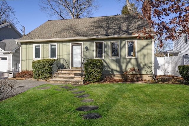 view of front of house with a chimney, roof with shingles, fence, board and batten siding, and a front yard