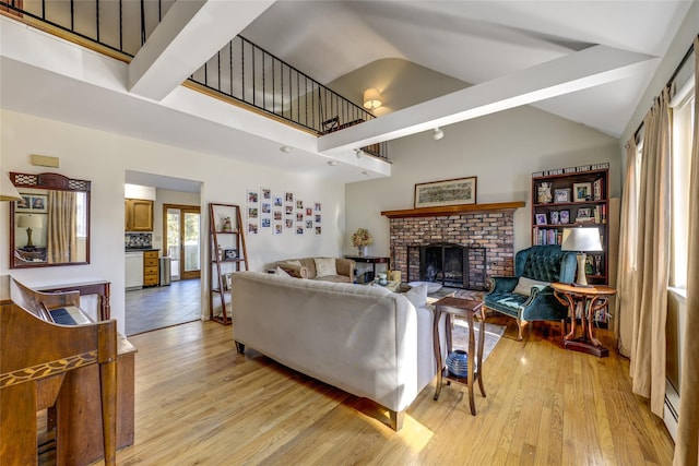 living area with a baseboard heating unit, high vaulted ceiling, light wood-type flooring, and a brick fireplace