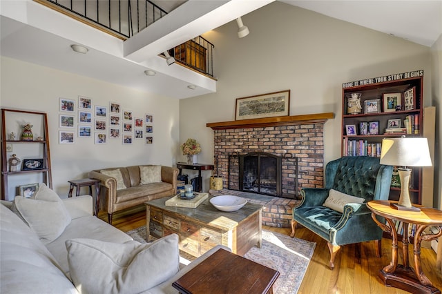 living room with high vaulted ceiling, a brick fireplace, and wood finished floors