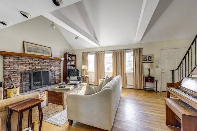 living room featuring a baseboard radiator, light wood-style flooring, vaulted ceiling, stairway, and a brick fireplace