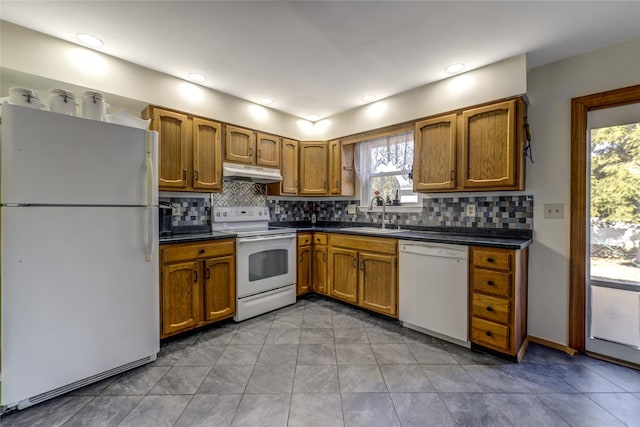 kitchen featuring white appliances, dark countertops, a sink, and under cabinet range hood