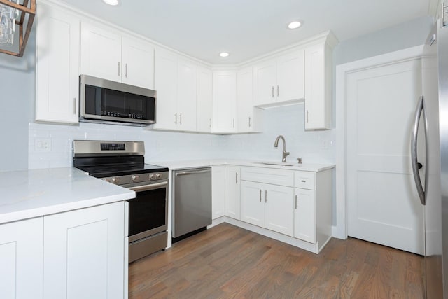 kitchen featuring tasteful backsplash, dark wood-type flooring, stainless steel appliances, white cabinetry, and a sink