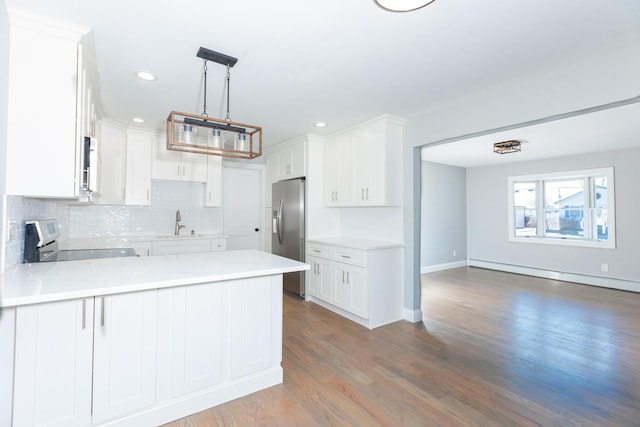 kitchen with decorative backsplash, baseboard heating, appliances with stainless steel finishes, a sink, and a peninsula