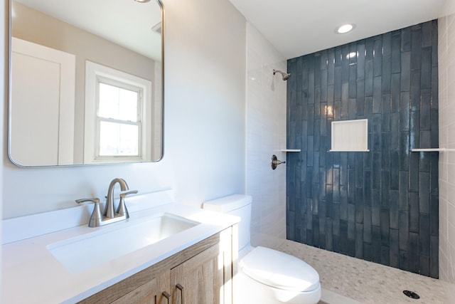 bathroom with tiled shower, vanity, and toilet