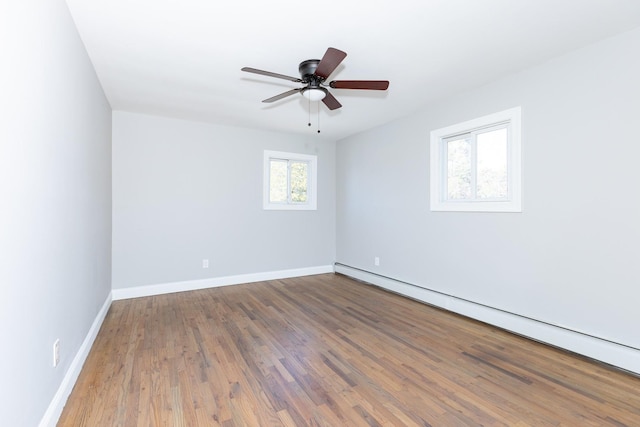 empty room featuring ceiling fan, baseboard heating, wood finished floors, and baseboards