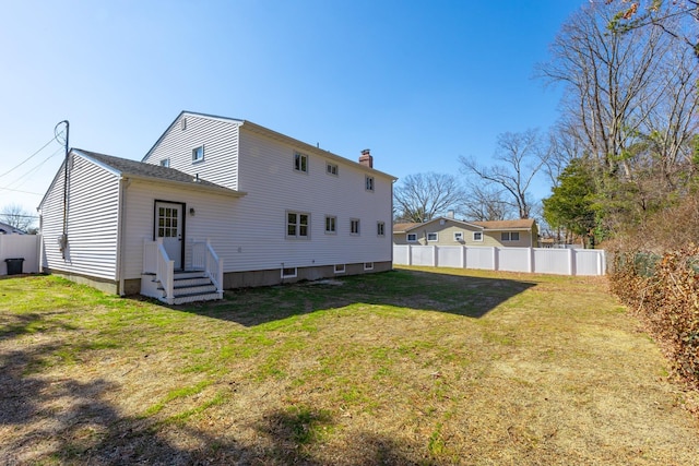 back of property featuring entry steps, a yard, a chimney, and fence