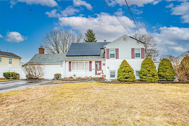 tri-level home featuring roof mounted solar panels, a chimney, fence, and a front yard