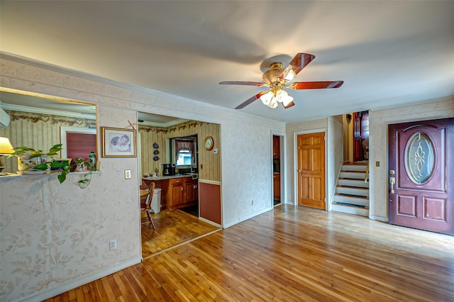 interior space with crown molding, wood-type flooring, stairway, baseboards, and wallpapered walls