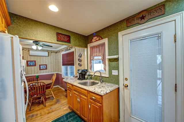 kitchen featuring a sink, a ceiling fan, freestanding refrigerator, brown cabinetry, and wallpapered walls