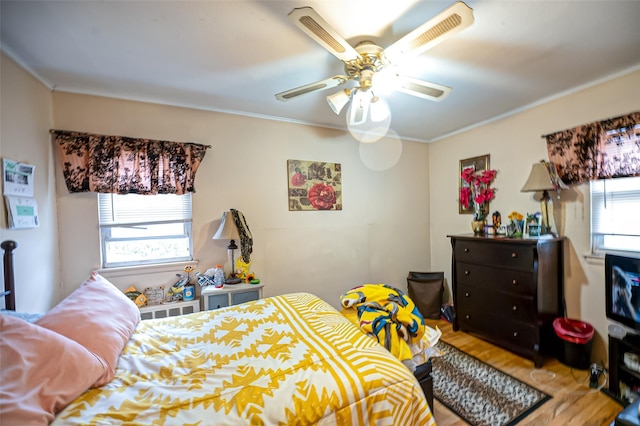 bedroom with ceiling fan, wood finished floors, visible vents, and crown molding