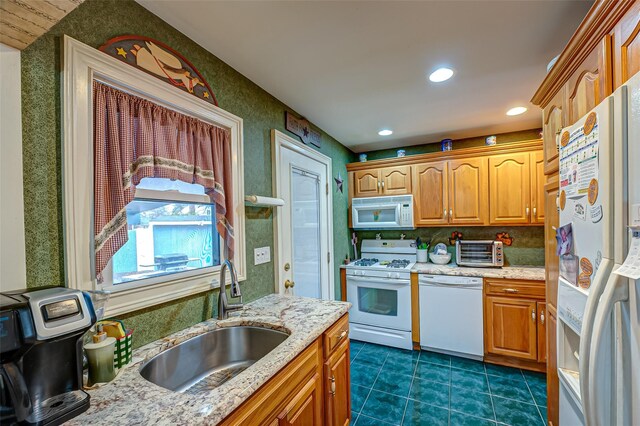 kitchen with white appliances, a toaster, light stone counters, dark tile patterned floors, and a sink