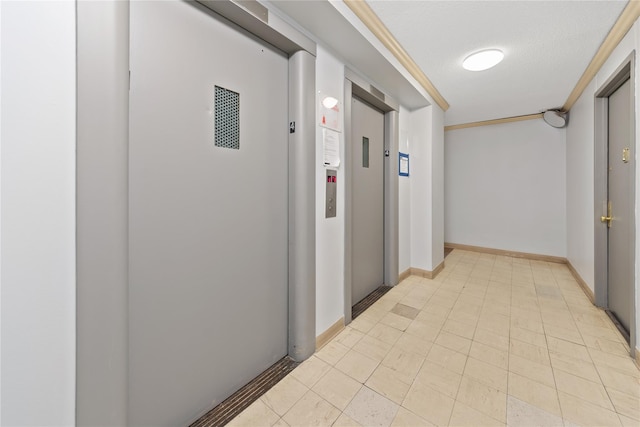 hallway featuring elevator, a textured ceiling, and baseboards