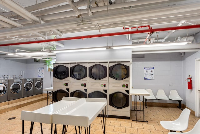 shared laundry area with independent washer and dryer, tile patterned floors, concrete block wall, and stacked washer / drying machine