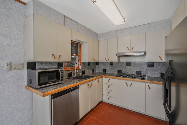 kitchen featuring cream cabinets, decorative backsplash, appliances with stainless steel finishes, a sink, and under cabinet range hood