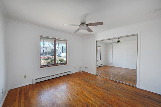 unfurnished bedroom featuring a baseboard heating unit, wood-type flooring, ornamental molding, and baseboards