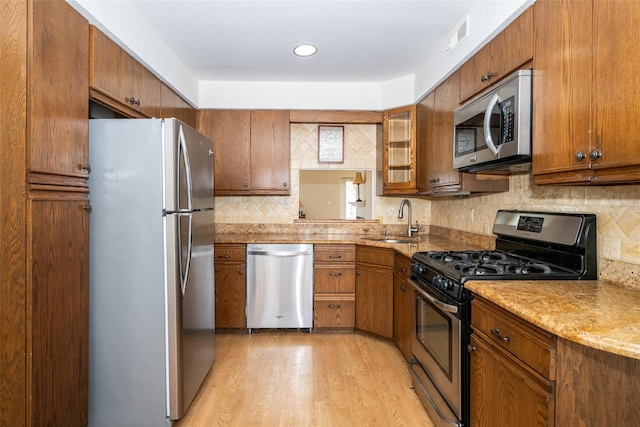 kitchen featuring brown cabinetry, a sink, appliances with stainless steel finishes, light wood-type flooring, and backsplash