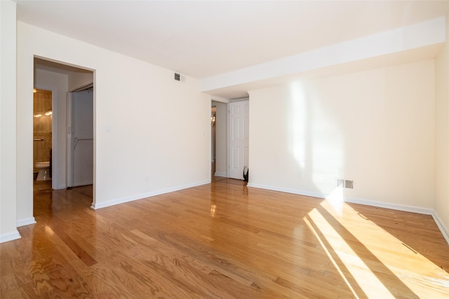 empty room with light wood-type flooring, visible vents, and baseboards