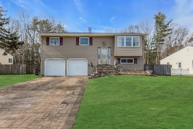 bi-level home featuring a garage, decorative driveway, a front yard, and fence