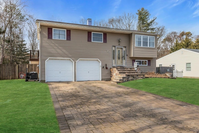 split foyer home with a garage, decorative driveway, fence, and a front lawn