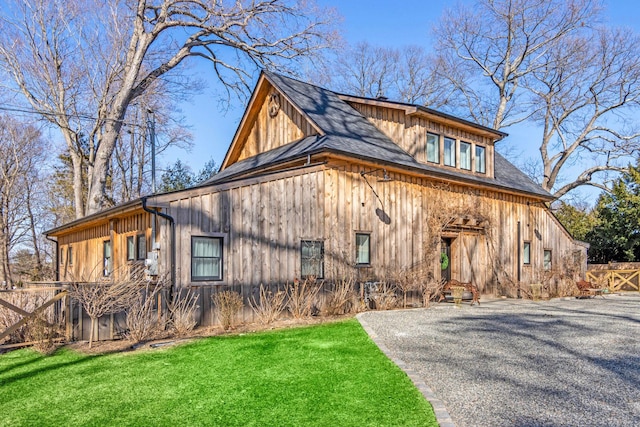 view of side of property featuring driveway, board and batten siding, fence, and a lawn