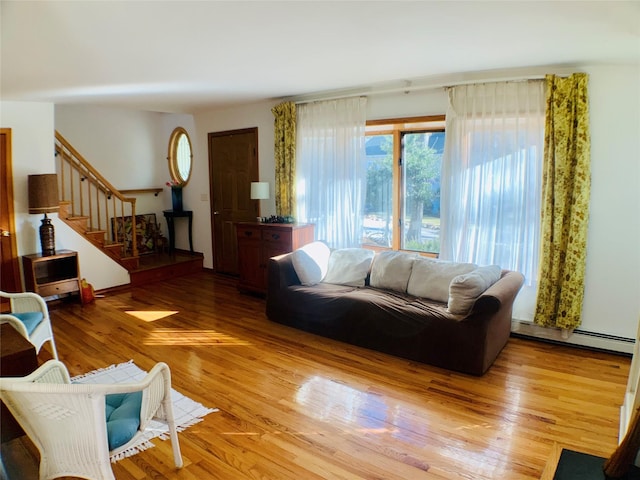 living area featuring a baseboard radiator, light wood finished floors, and stairs