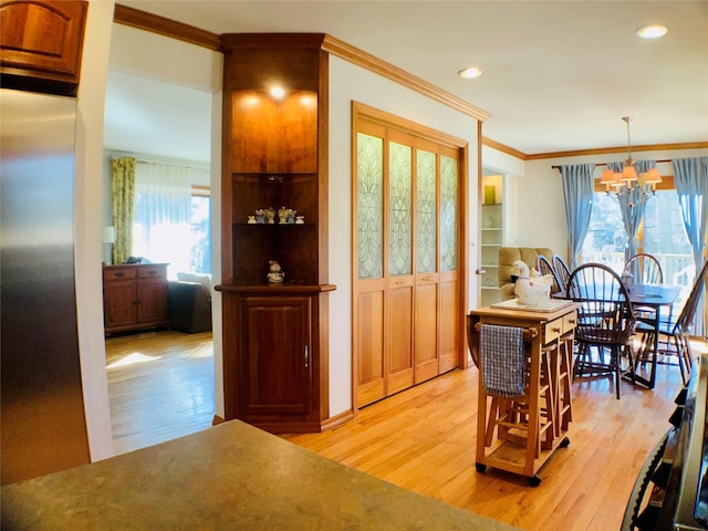 dining room featuring crown molding, a healthy amount of sunlight, an inviting chandelier, and light wood-style floors