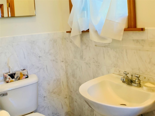 bathroom featuring toilet, tile walls, and a sink