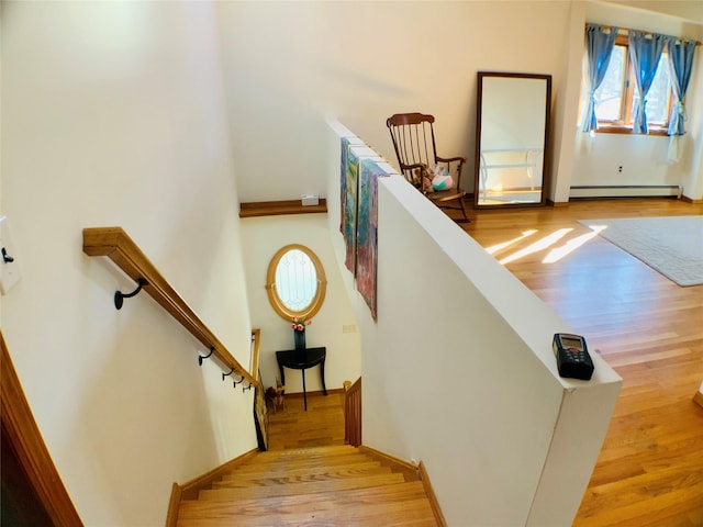 staircase featuring a baseboard heating unit and wood finished floors