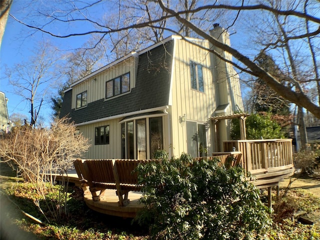 exterior space featuring a shingled roof, a chimney, a wooden deck, and a gambrel roof