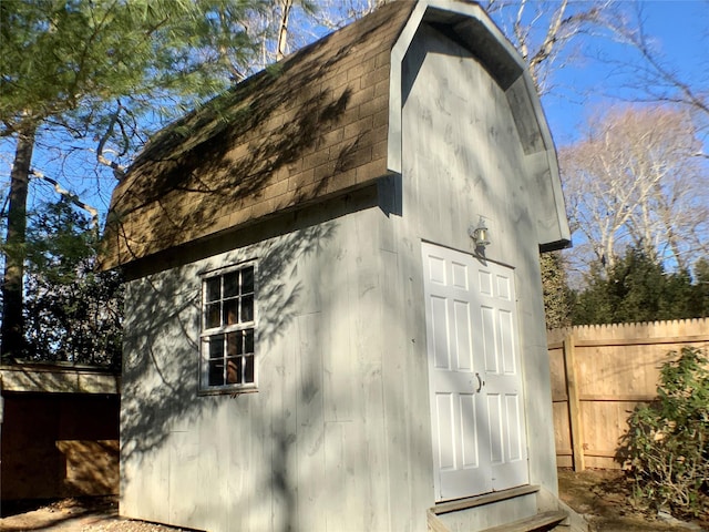 view of property exterior featuring a shingled roof, an outbuilding, fence, and a gambrel roof