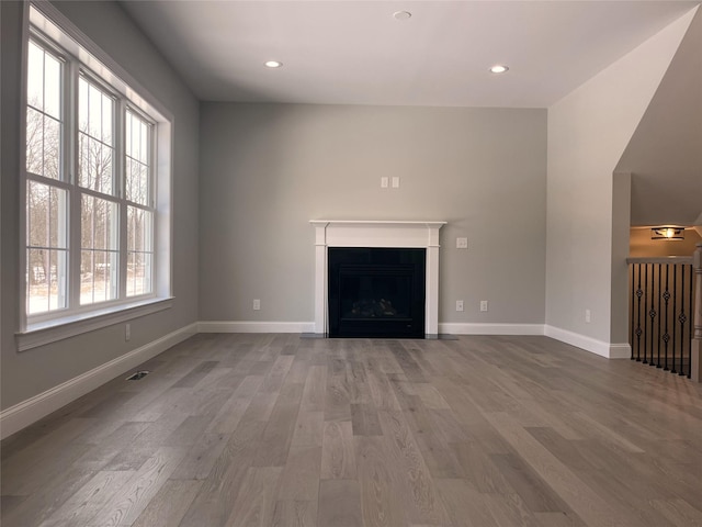 unfurnished living room featuring a fireplace with flush hearth, recessed lighting, baseboards, and wood finished floors