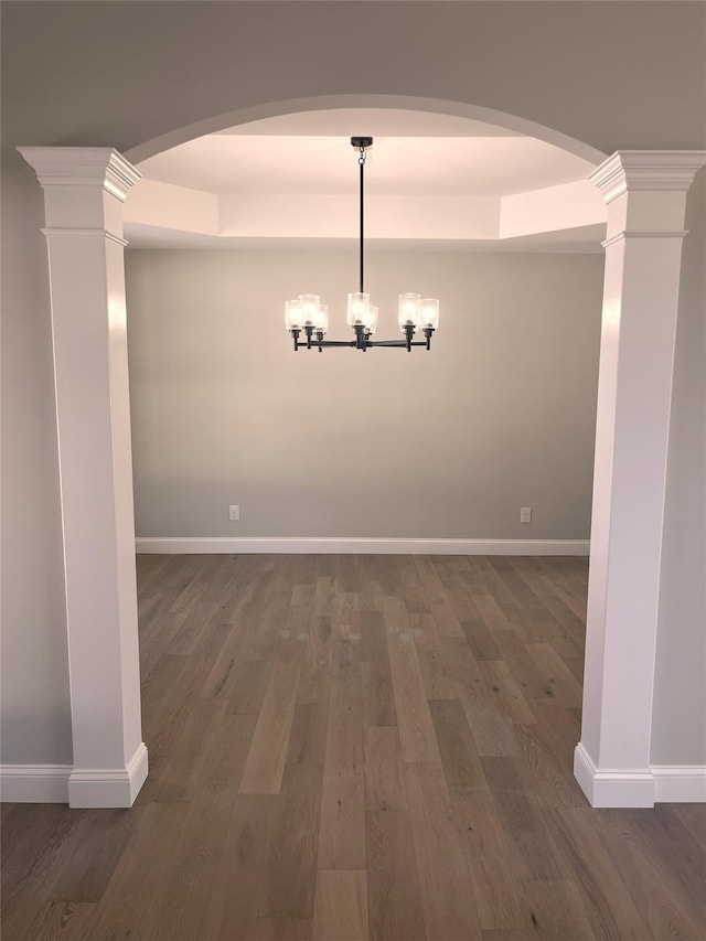 unfurnished dining area featuring dark wood-style floors, decorative columns, baseboards, and a chandelier