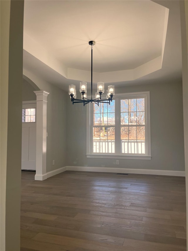 unfurnished dining area featuring a tray ceiling, a notable chandelier, dark wood finished floors, and baseboards