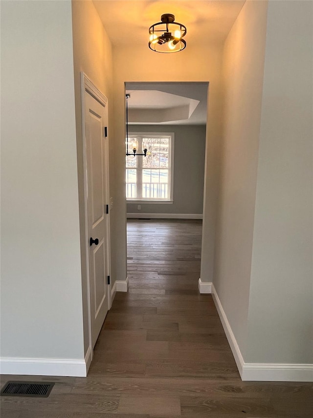 corridor featuring a tray ceiling, dark wood finished floors, visible vents, and baseboards