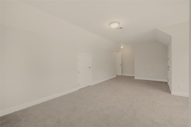 additional living space featuring baseboards, visible vents, vaulted ceiling, and light colored carpet