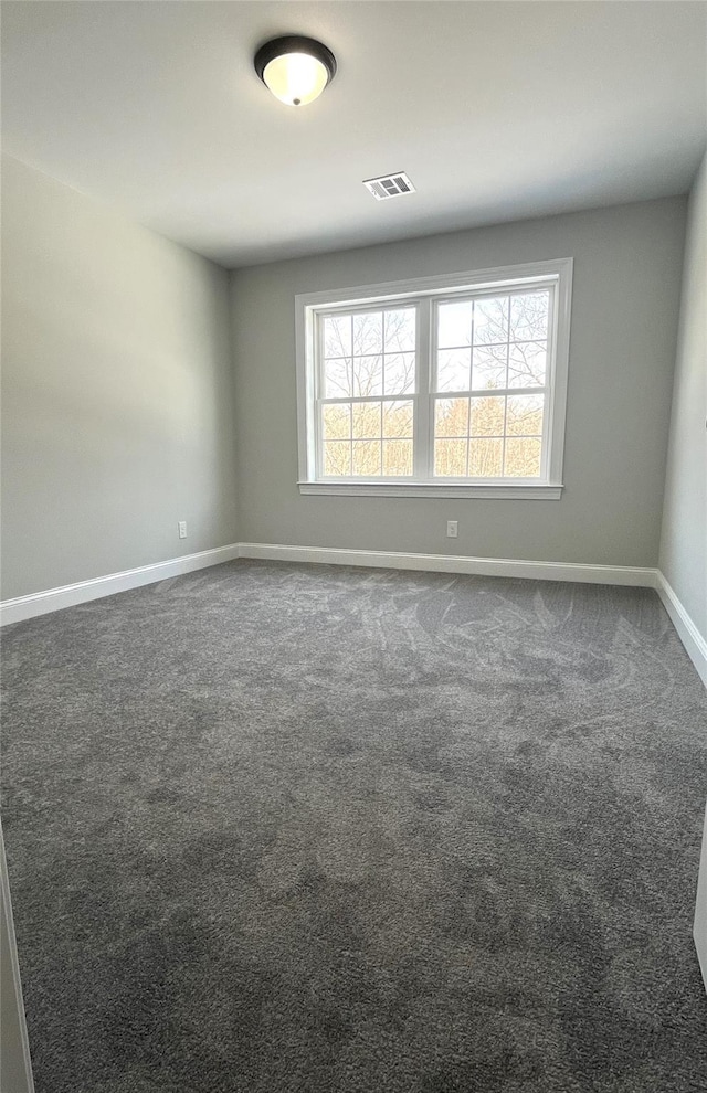 unfurnished room with dark colored carpet, visible vents, plenty of natural light, and baseboards