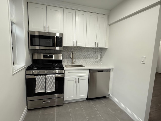 kitchen with stainless steel appliances, light countertops, backsplash, white cabinets, and a sink