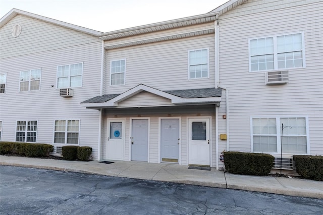 townhome / multi-family property with a shingled roof and a wall unit AC