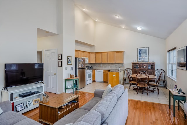 living room with high vaulted ceiling, light wood-type flooring, and baseboards