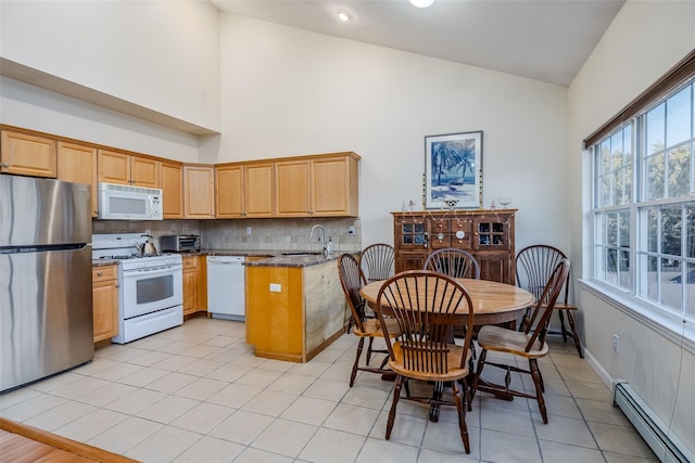 kitchen featuring a baseboard heating unit, a peninsula, white appliances, a sink, and backsplash