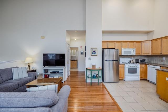 kitchen with open floor plan, white appliances, backsplash, and a high ceiling