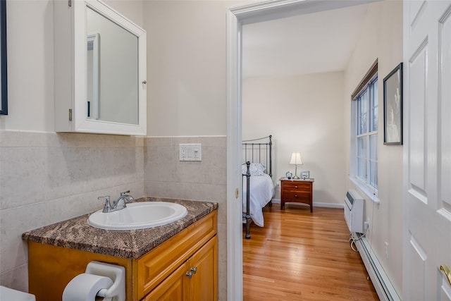 ensuite bathroom featuring a wall unit AC, tasteful backsplash, baseboard heating, vanity, and wood finished floors