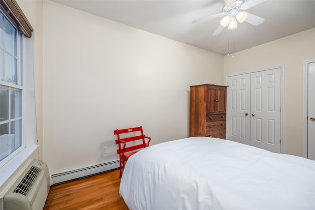 bedroom featuring a ceiling fan, a baseboard radiator, wood finished floors, a closet, and a wall mounted AC