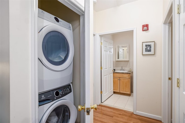 laundry room featuring light wood-type flooring, stacked washer / dryer, a sink, and baseboards