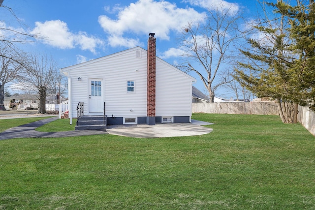 rear view of house featuring entry steps, a lawn, a patio, a chimney, and fence