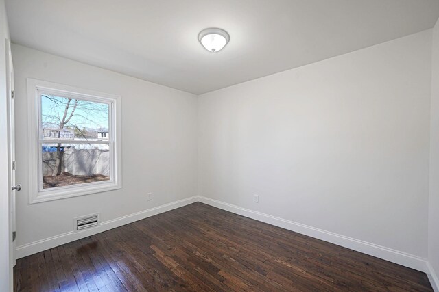 unfurnished room with dark wood-style flooring, visible vents, and baseboards