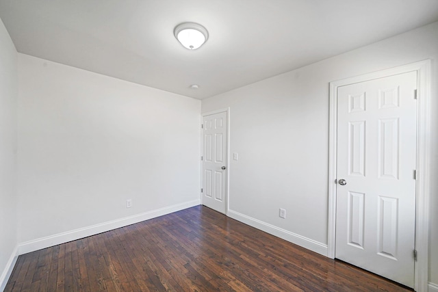 empty room featuring baseboards and dark wood-type flooring