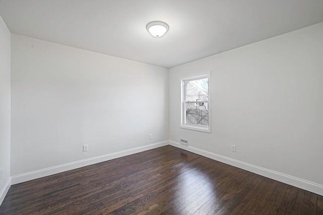 spare room with baseboards, visible vents, and dark wood-style flooring