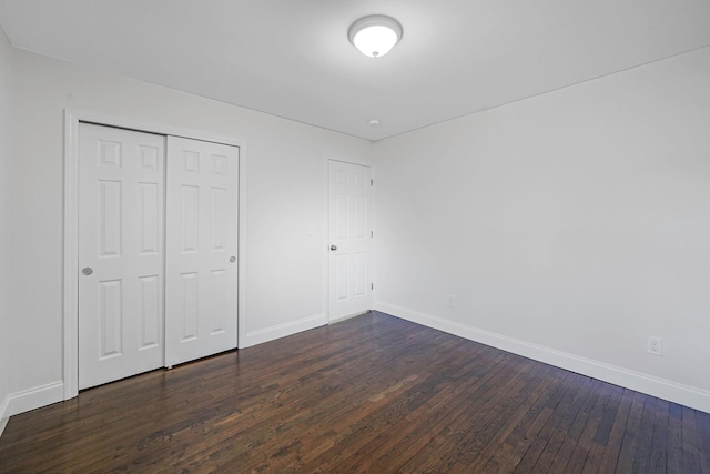 unfurnished bedroom with dark wood-type flooring, a closet, and baseboards